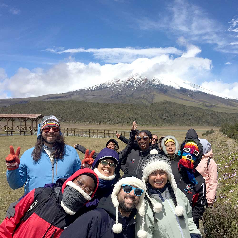 warmly dressed group of smiling students and teachers with a smoky volcano in the background